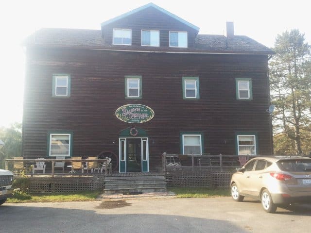 brown cabin with white windows and green borders, patio in front with white lawn chairs, gold car parked in front